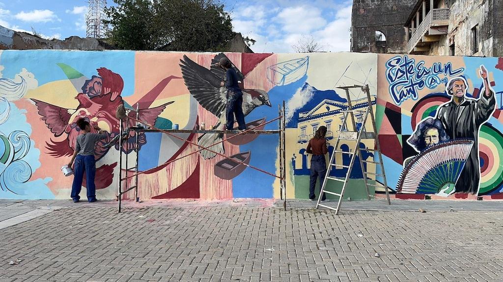 ES: Mujeres pintando un ave y arquitectura en el muro. FR: Femmes peignant un oiseau et de l'architecture sur le mur. EN: Women painting a bird and architecture on the wall.