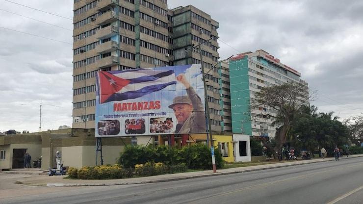 ES: Afiche en Matanzas, Cuba, con la bandera y Fidel Castro frente a edificios altos.
FR: Panneau à Matanzas, Cuba, avec drapeau et Fidel Castro devant de grands immeubles.EN: Billboard in Matanzas, Cuba, featuring the flag and Fidel Castro before tall buildings.